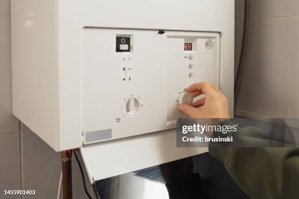 a woman reduces the power of the gas boiler in her home due to an energy crisis - caldeira imagens e fotografias de stock