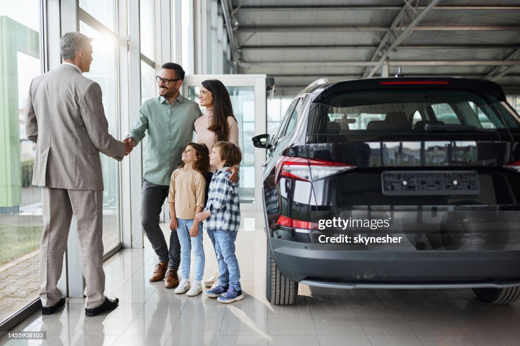 Junge glückliche Familie schüttelt einem Autoverkäufer in einem Showroom die Hand.