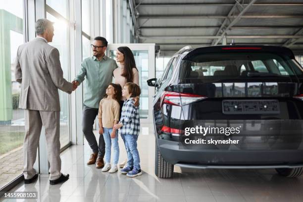 young happy family shaking hands with a car salesperson in a showroom. - new 個照片及圖片檔
