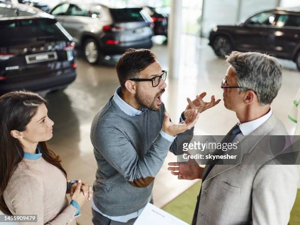 frustrated couple arguing with car salesperson in a showroom. - car salesman stock pictures, royalty-free photos & images