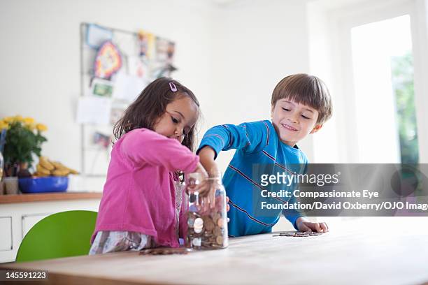 children putting coins into jar - jarred stock pictures, royalty-free photos & images
