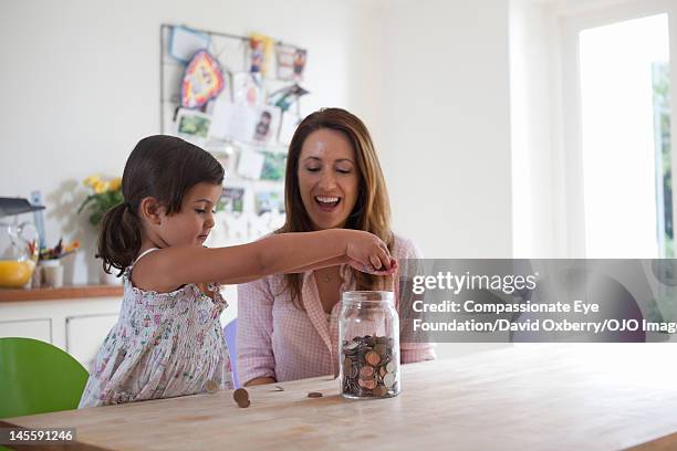 mother and daughter (3-4) putting coins into jar - child saving stock pictures, royalty-free photos & images