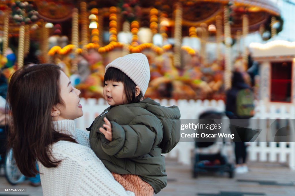 Cheerful young Asian mother and toddler at funfair