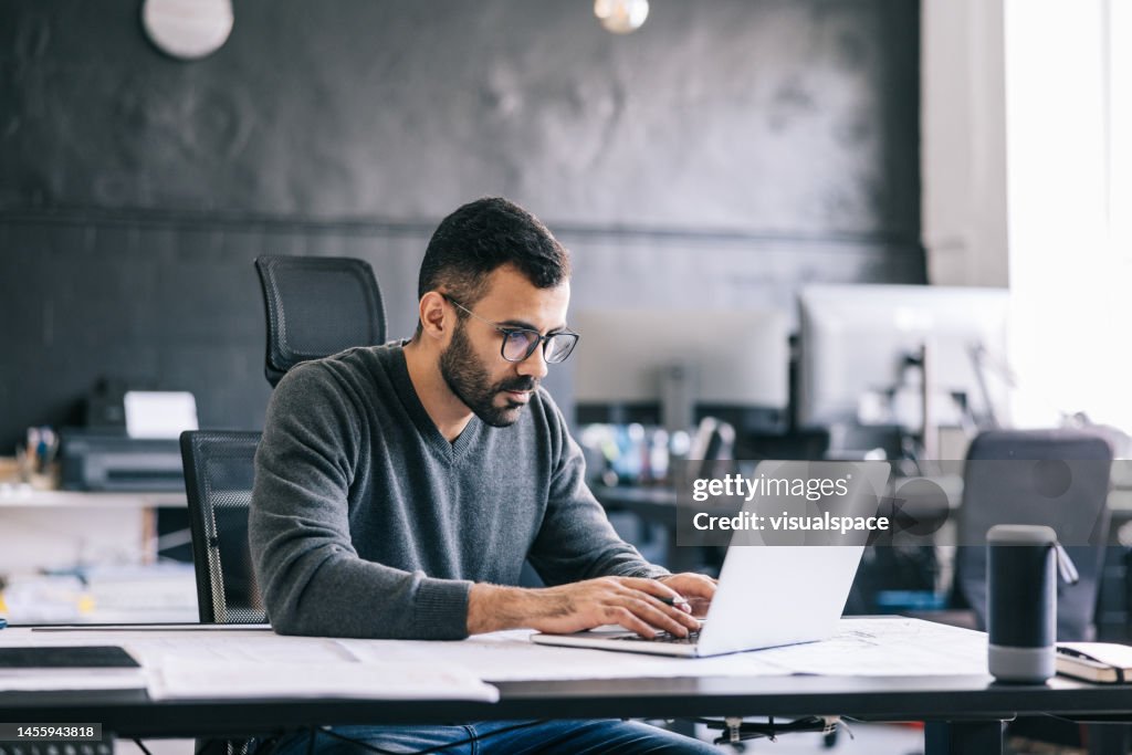 The architect takes notes on the blueprint, then inputs them into the laptop to keep an digital record of the design process.