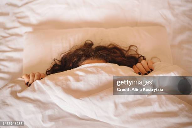 angry woman hides under white blanket, only her long  curly hair and dark manicured hands are visible. - curly brown hair stock pictures, royalty-free photos & images