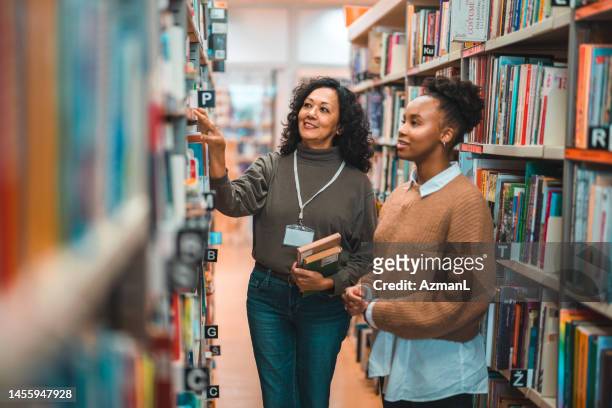mid adult hispanic bibliothekar begleitet einen studenten in einer bibliothek - librarian stock-fotos und bilder