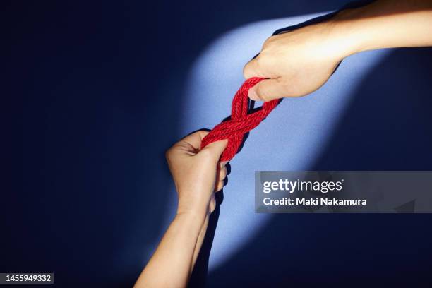 the hand holding the bundle of red thread is illuminated by a spotlight. - 調布 stockfoto's en -beelden