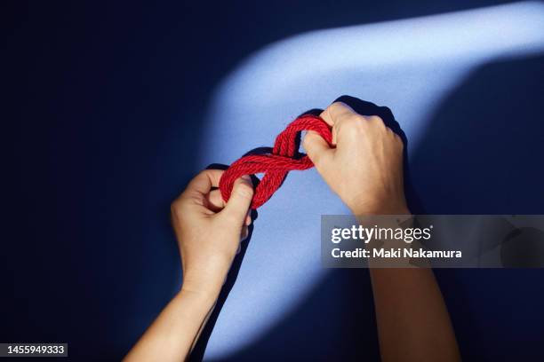 the hand holding the bundle of red thread is illuminated by a spotlight. - 調布 fotografías e imágenes de stock