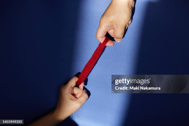 the hand holding the bundle of red thread is illuminated by a spotlight. - 調布 fotografías e imágenes de stock