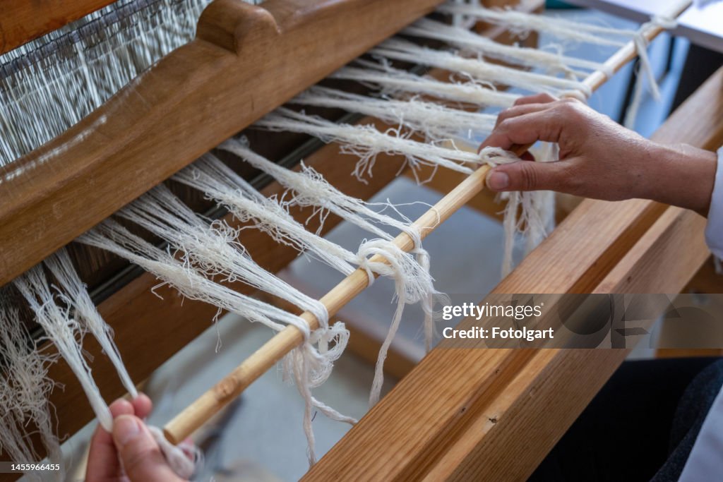Hands weaving threads at a loom.