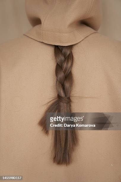 a braid of hair on the back of a young woman. the braid peeks out from under the hood on a beige background. hairstyle of brown hair with copy space. - beautiful braid stockfoto's en -beelden