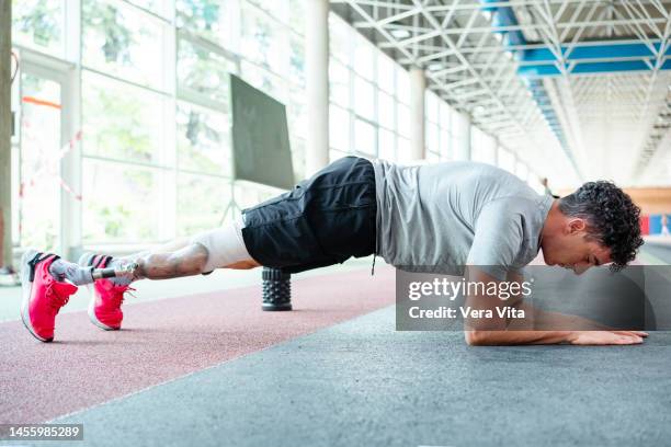 full length view of young man with prosthetic leg doing flat crunches on stadium indoors. - vita shorts fotografías e imágenes de stock