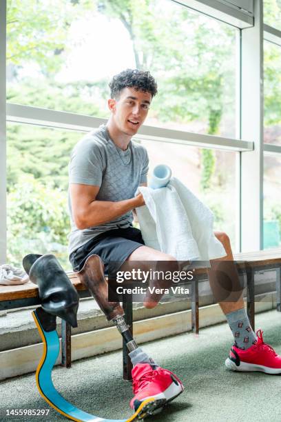 full length view of caucasian young man with leg stump cleaning and changing professional prosthesis leg at gym indoors - vita shorts fotografías e imágenes de stock