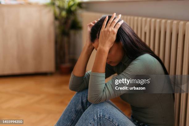 sad young woman sitting on the floor at home - overstuur stockfoto's en -beelden