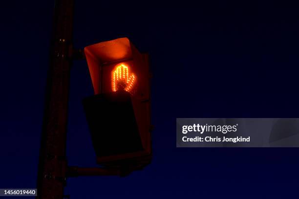 lit orange "don't walk" hand sign icon at road intersection - stop stock-fotos und bilder