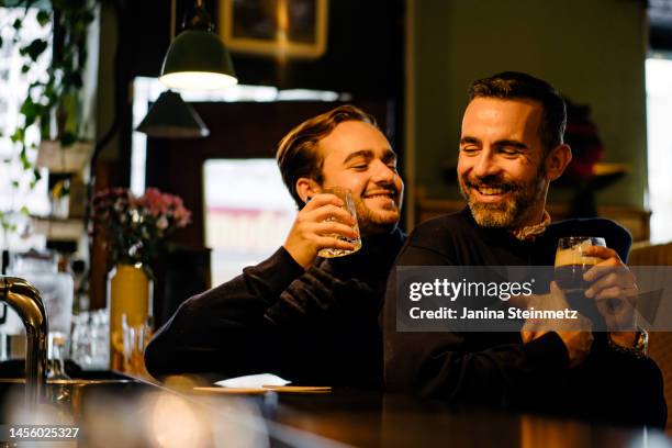two men laughing at warm and inviting bar - gay bar stock pictures, royalty-free photos & images