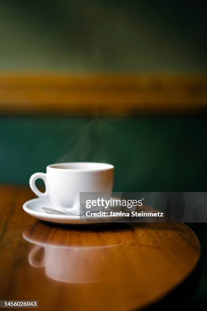 steaming white coffee cup sitting on rich wood cafe table in cafe - tasse à café photos et images de collection