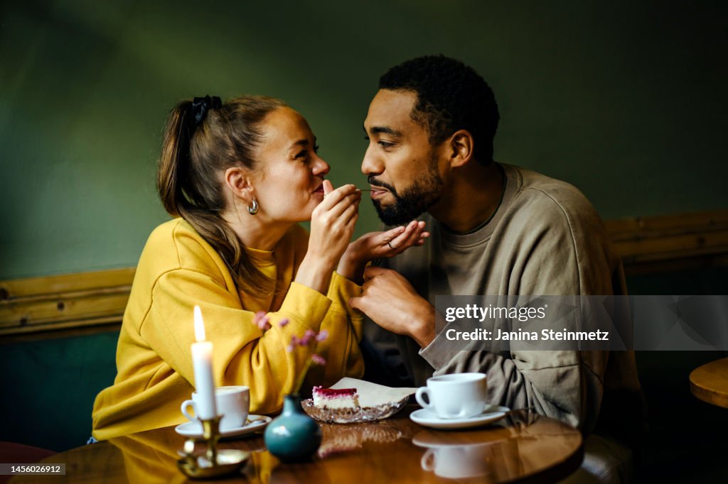 Girlfriend feeding bite of dessert to her boyfriend at cafe