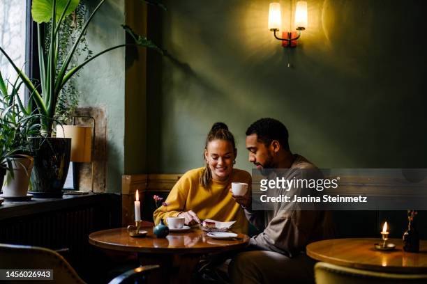 wide shot with copy space of couple sharing a dessert in cafe - multiracial couple fotografías e imágenes de stock
