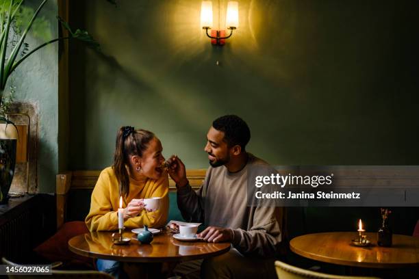 wide shot of boyfriend feeding girlfriend a bite of dessert - couples romance stock-fotos und bilder