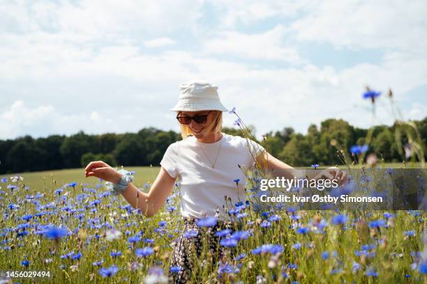 jeune femme dans une mer de bleuets bleus - femme au chapeau fleuri photos et images de collection