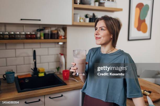 hermosa mujer en forma bebiendo batido mientras está de pie en la cocina - batiendo fotografías e imágenes de stock