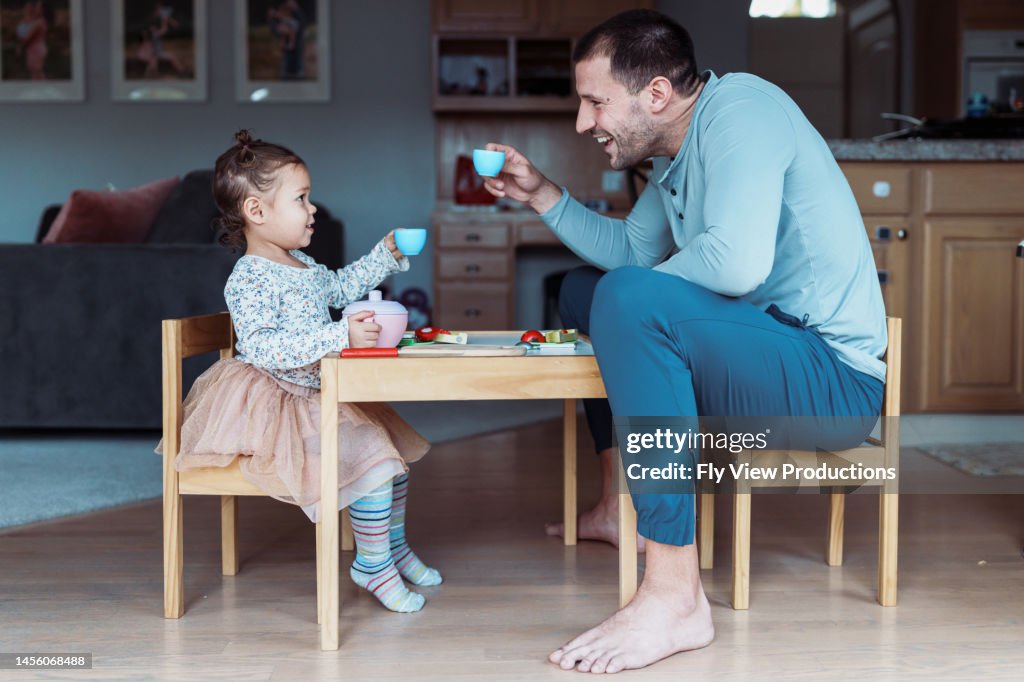 Toddler girl and dad toast while having tea party