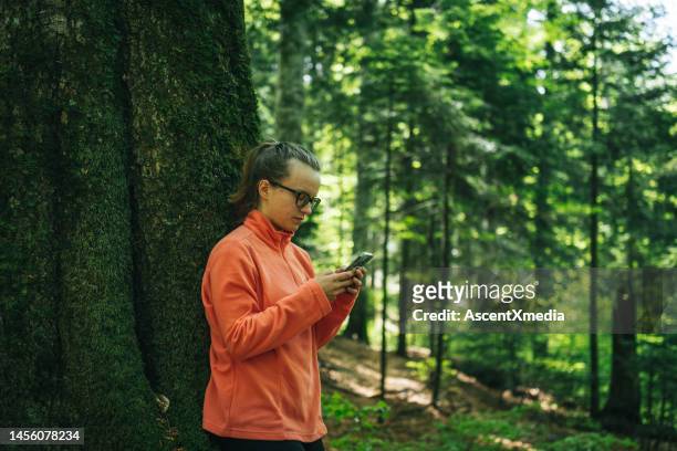 young woman uses mobile phone in forest - escape rom stock pictures, royalty-free photos & images