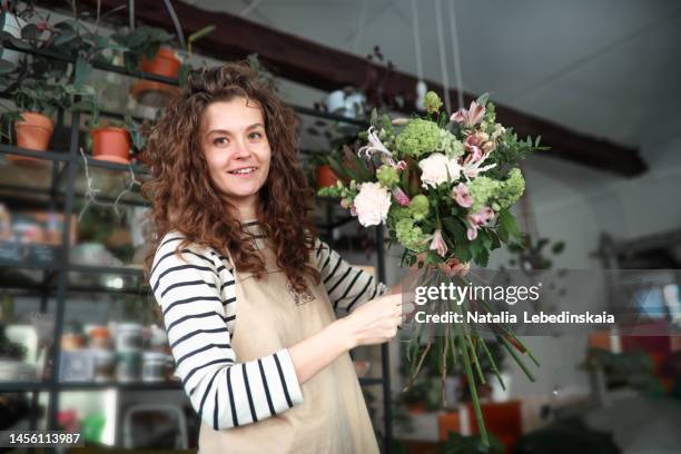 owner of small flower shop makes delicate stylish bouquet of fresh flowers. looking at camera. - florist arranging stock pictures, royalty-free photos & images