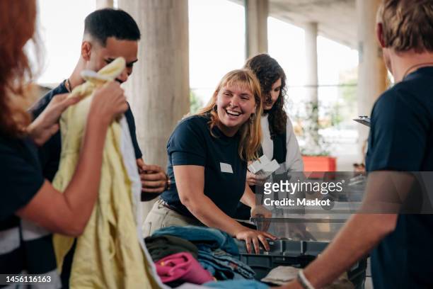 happy female volunteer looking at colleague while sorting clothes at community service center - soziale verantwortung stock-fotos und bilder