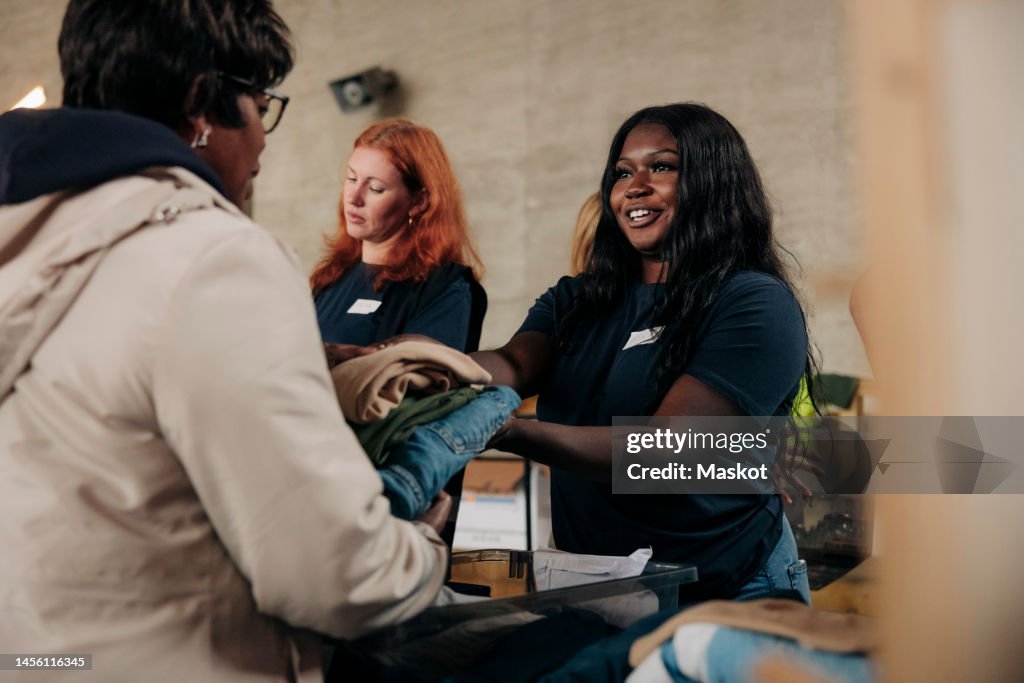 Smiling female volunteer giving donated clothes to homeless woman at community center
