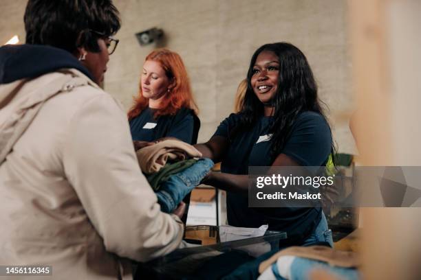 smiling female volunteer giving donated clothes to homeless woman at community center - homelessness stock pictures, royalty-free photos & images