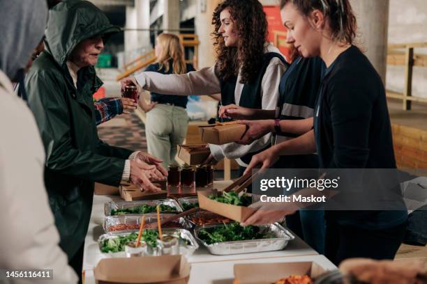 homeless people collecting food from volunteers at community center - volunteer food stock pictures, royalty-free photos & images