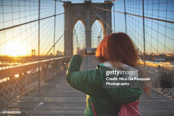 woman taking picture on the brooklyn bridge at dawn. new york city - the bigger picture stock photos et images de collection