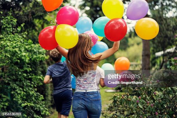 glückliche drei teenager mit luftballons, die im hinterhof laufen - kids party balloons stock-fotos und bilder