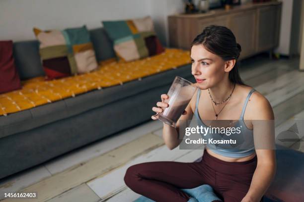 a fit woman drinks a milkshake while sitting on an exercise mat in the living room - milkshake bildbanksfoton och bilder