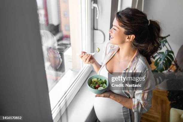 pregnant woman eating healthy food and salads looking through window - pregnancy healthy eating stock pictures, royalty-free photos & images