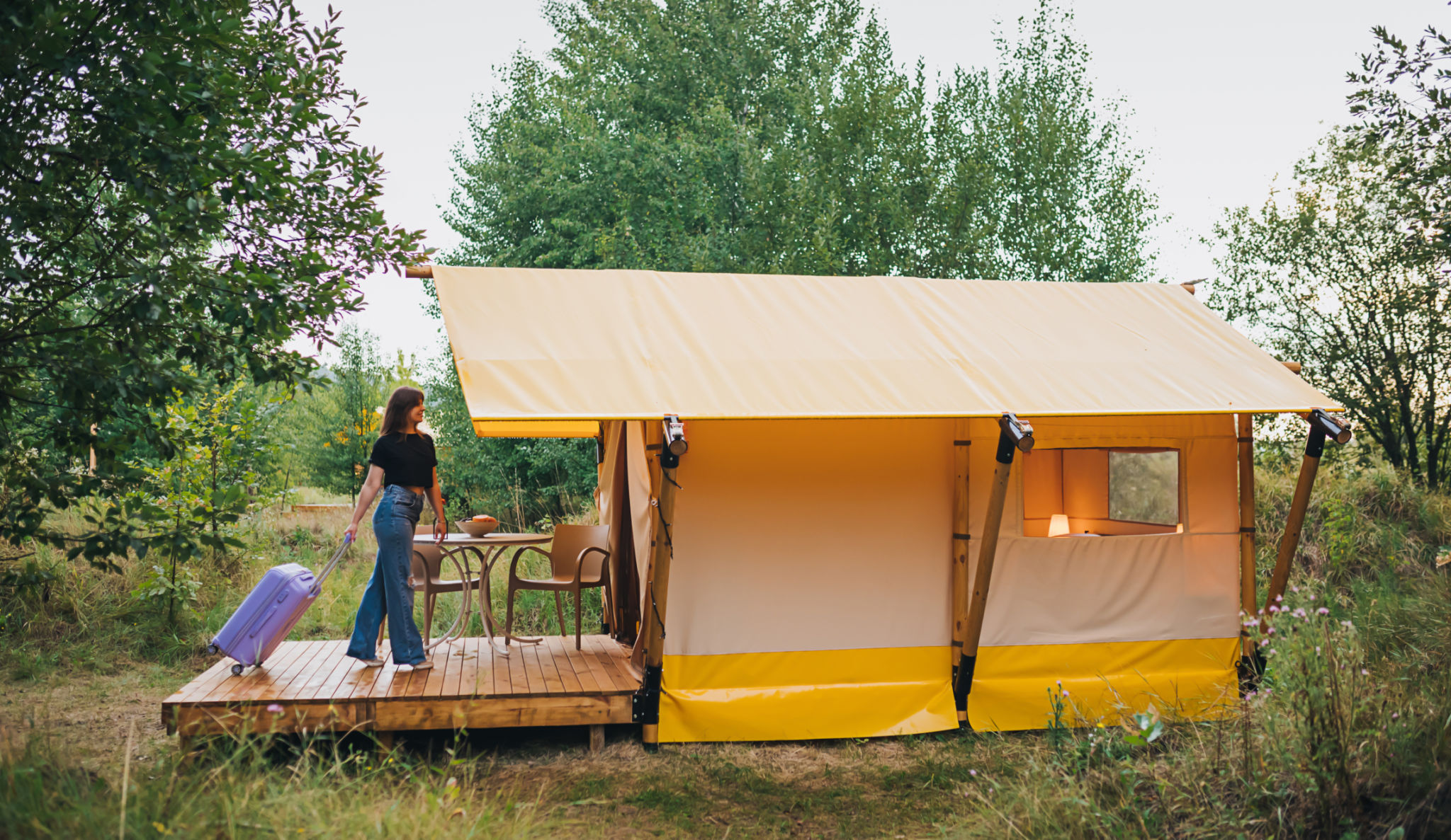 Woman traveler with luggage moving towards bedroom of cozy glamping house. Luxury camping tent for outdoor summer holiday and vacation. Lifestyle concept Woman traveler with luggage moving towards bedroom of cozy glamping house. Luxury camping tent for outdoor summer holiday and vacation. Lifestyle concept