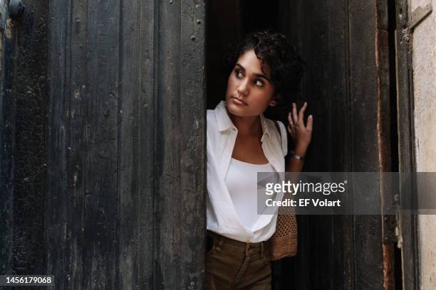 beautiful hispanic woman going out, opening wooden door and peeking out the house looking the street - man opening door woman stock-fotos und bilder