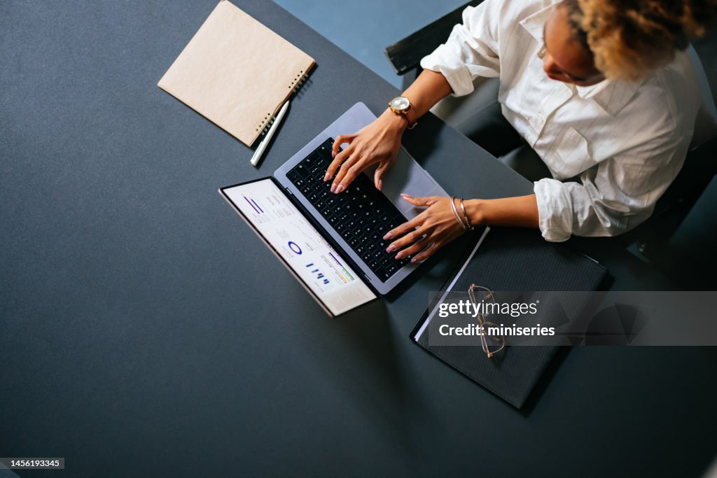 Hohe Winkelansicht einer nicht erkennbaren Frau, die Geschäftsbericht auf einer Laptop-Tastatur im Café eintippt