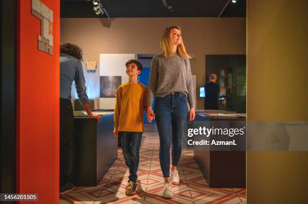 beautiful blond woman entering the museum room with her black-haired son - family museum stock pictures, royalty-free photos & images