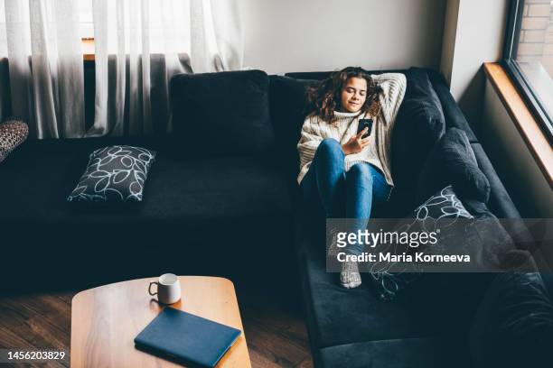 woman using smart phone for social media laying in her couch. - movie still stock-fotos und bilder