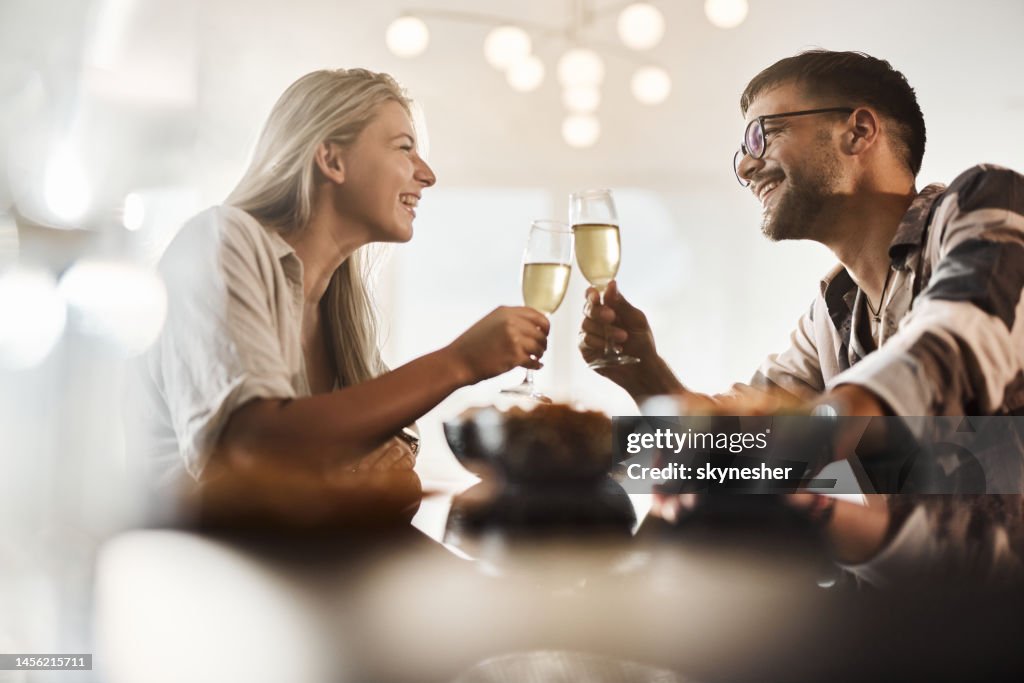 Junges glückliches Paar, das zu Hause mit Champagner anstößt.