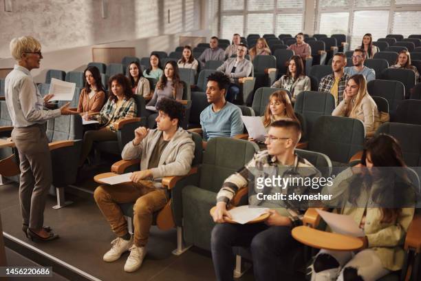college-studenten hören ihrem leitenden lehrer in einer klasse im hörsaal zu. - lecture theatre stock-fotos und bilder