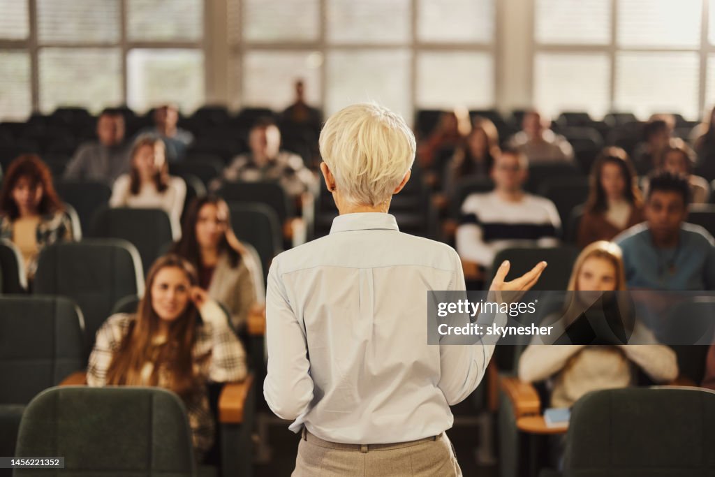 Back view of a female professor teaching her students at lecture hall.