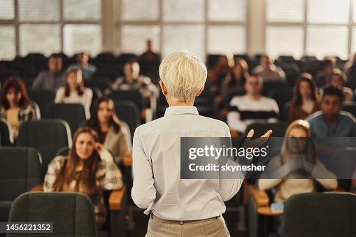 Back view of a female professor teaching her students at lecture hall. Back view of a female professor teaching her students at lecture hall.