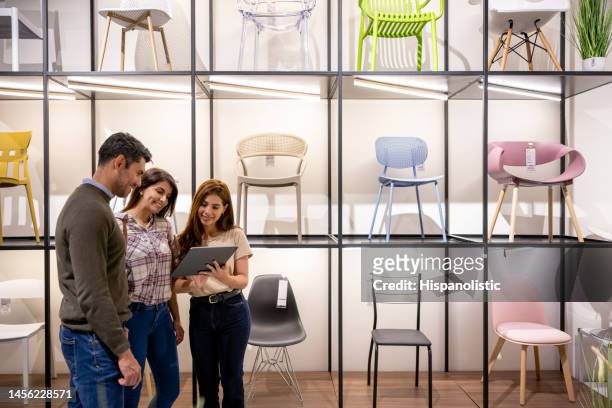 retail clerk helping a couple buying chairs at a furniture store - furniture store stockfoto's en -beelden