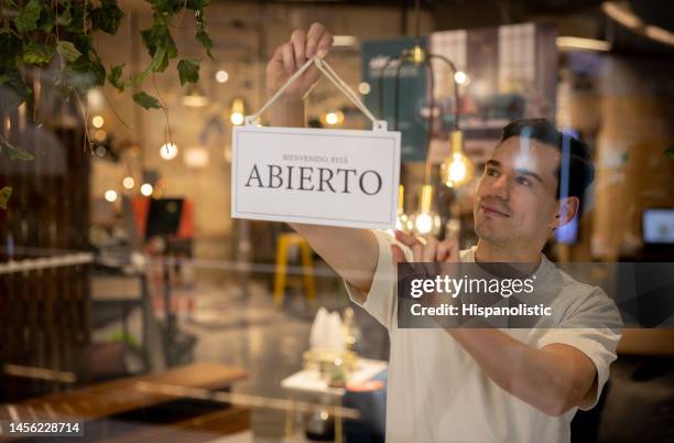 家具店のドアに開いた看板をぶら下げる小売店員 - スペイン語 ストックフォトと画像