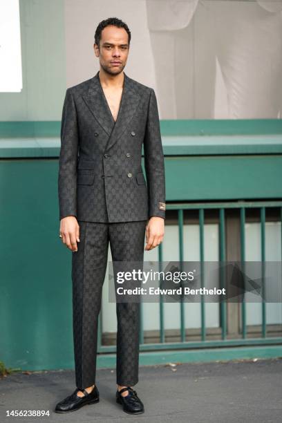 Raven Smith wears a gray embroidered monogram blazer jacket from Gucci, matching dark gray embroidered monogram suit pants from Gucci, black shiny...