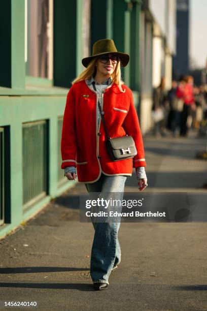 Guest wears a khaki felt / wool hat, brown sunglasses, a blue denim shirt, a white cut-out wool pullover, a red felt buttoned cardigan jacket, a...